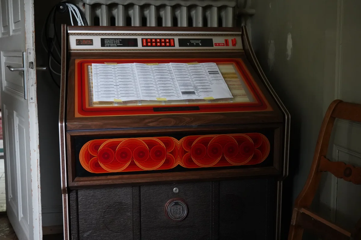 Eine alte rot-braune Box zum Musikabspielen steht in einer Ecke eines Zimmers. 